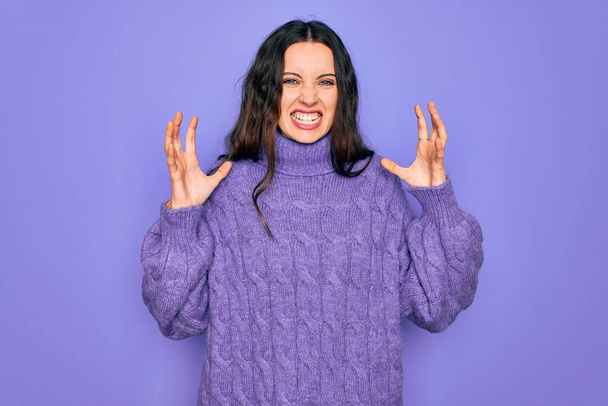 Young beautiful woman wearing casual turtleneck sweater standing over purple background Shouting frustrated with rage, hands trying to strangle, yelling mad - Φωτογραφία, εικόνα