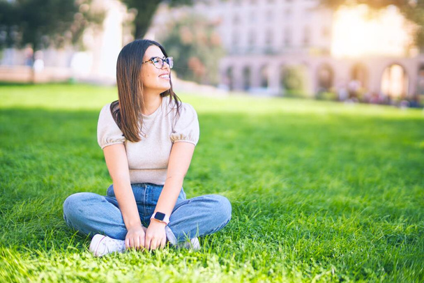 Young beautiful woman smiling happy and confident. Sitting on the grass with smile on face at park - Photo, image