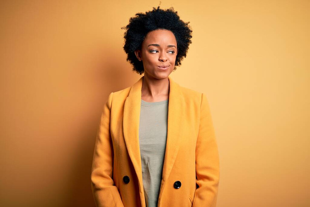Young beautiful African American afro businesswoman with curly hair wearing yellow jacket smiling looking to the side and staring away thinking. - Foto, immagini