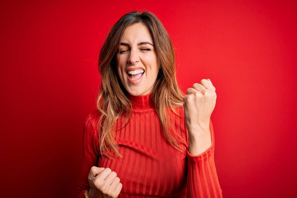Young beautiful brunette woman wearing casual turtleneck sweater over red background celebrating surprised and amazed for success with arms raised and eyes closed. Winner concept. - Foto, Bild
