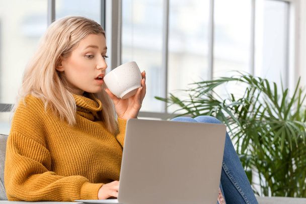 Kaunis nuori nainen kannettavan tietokoneen juominen teetä kotona - Valokuva, kuva