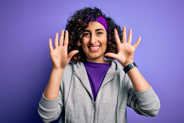 Linda esportista árabe encaracolado fazendo esporte vestindo sportswear sobre fundo roxo mostrando e apontando para cima com os dedos número dez, enquanto sorrindo confiante e feliz
. - Foto, Imagem