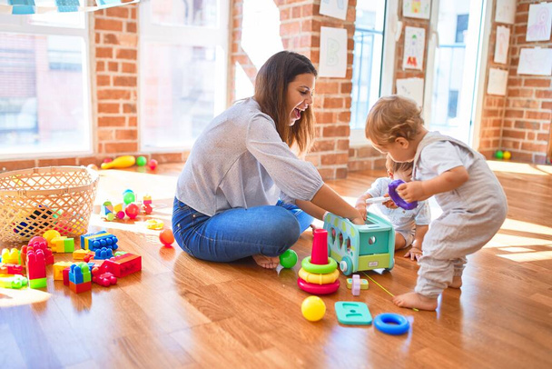 Beautiful teacher and toddlers playing around lots of toys at kindergarten - 写真・画像