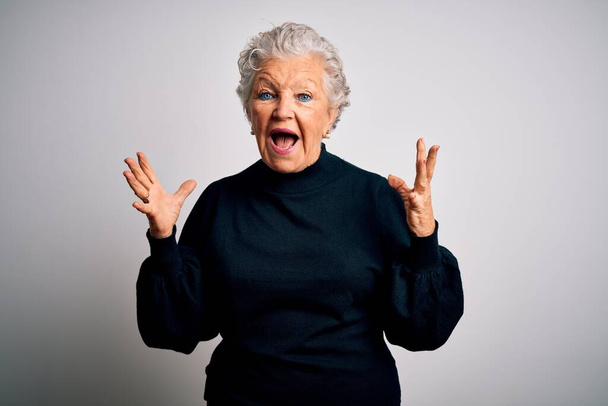 Senior beautiful woman wearing casual black sweater standing over isolated white background celebrating crazy and amazed for success with arms raised and open eyes screaming excited. Winner concept - Zdjęcie, obraz