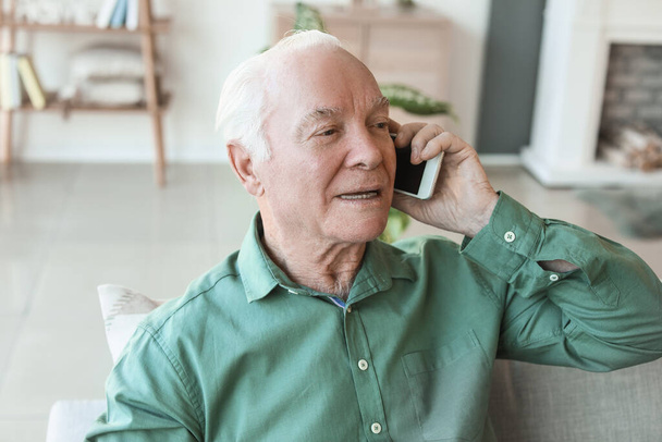 Oudere man in gesprek met mobiele telefoon thuis - Foto, afbeelding