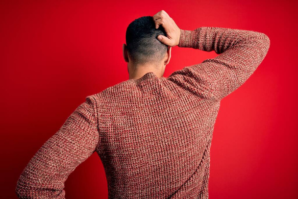 Joven hombre hispano guapo usando gafas nerd sobre fondo rojo hacia atrás pensando en la duda con la mano en la cabeza
 - Foto, Imagen