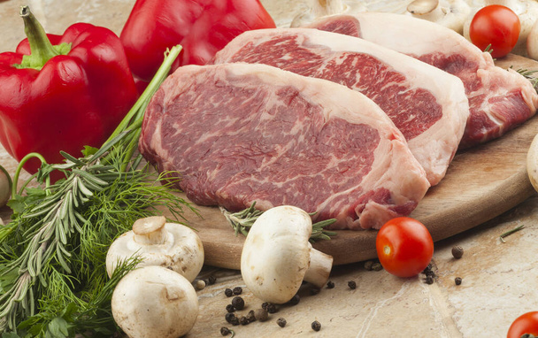 Raw fresh meat steak Ribeye marble greens, tomatoes and mushrooms on a plate, selective focus - Zdjęcie, obraz