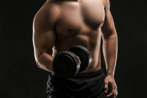 Sporty young man with dumbbell on dark background - 写真・画像