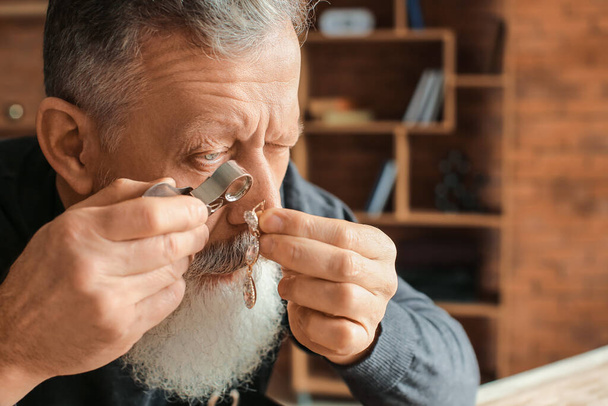 Jeweller examining adornment in workshop - Фото, изображение