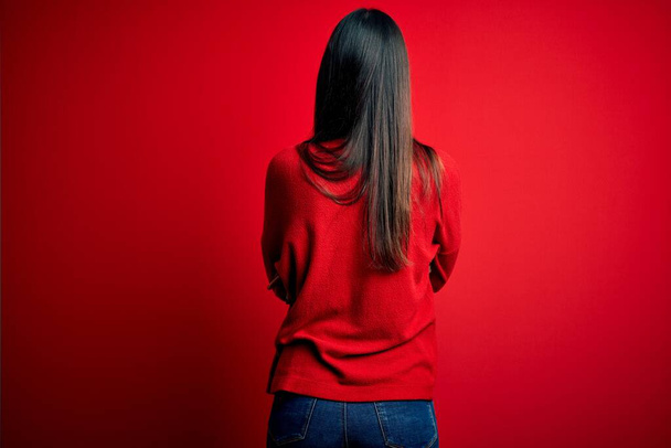 Joven mujer morena hermosa usando suéter casual sobre fondo rojo aislado de pie hacia atrás mirando hacia otro lado con los brazos cruzados
 - Foto, imagen
