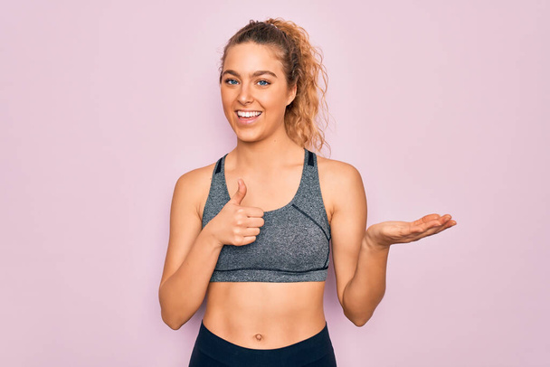 Young beautiful blonde sportswoman with blue eyes doing exercise wearing sportswear Showing palm hand and doing ok gesture with thumbs up, smiling happy and cheerful - Photo, Image