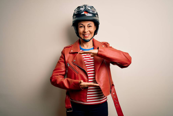 Жінка середнього віку мотоциклістка носить мотоциклетний шолом і піджак на білому тлі жестикулює руками, показуючи великий і великий розмір знак, мірний символ. Посміхаючись дивитися на камеру. Концепція вимірювання
. - Фото, зображення