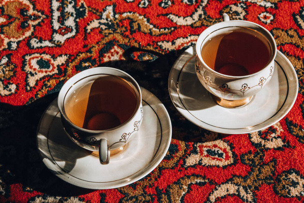 Two vintage porcelain cups of coffee or tea on the oriental turkish or asian carpet, tea ceremony, sunlight and deep shadow - Photo, Image