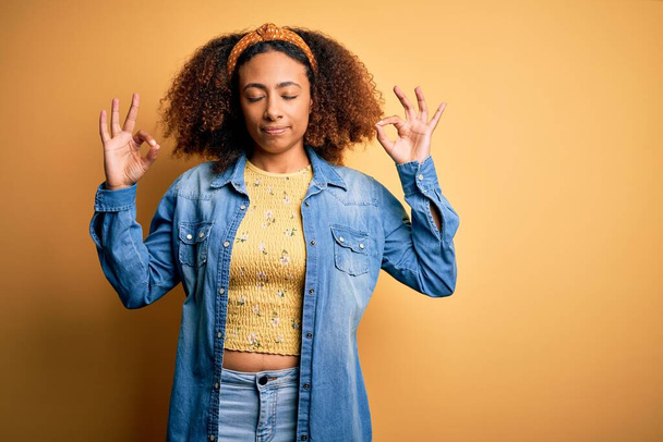 Gyönyörű afro-amerikai, afro haj áll sárga elszigetelt háttér pihenni, és mosolyogva csukott szemmel csinál meditációs gesztus ujjakkal. A jóga fogalma. - Fotó, kép