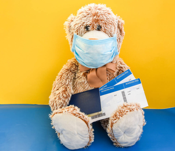 mackó játék visel orvosi arc maszk és birtokló nemzetközi útlevél és beszállókártya sárga háttér, másolja helyet a szöveges, karantén ellen coronavirus, utazás és covid-19 - Fotó, kép