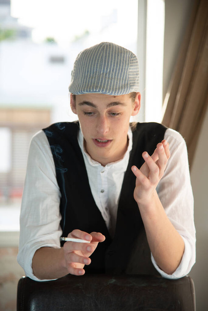 Un joven con gorra y chaleco fuma junto a la ventana
 - Foto, Imagen