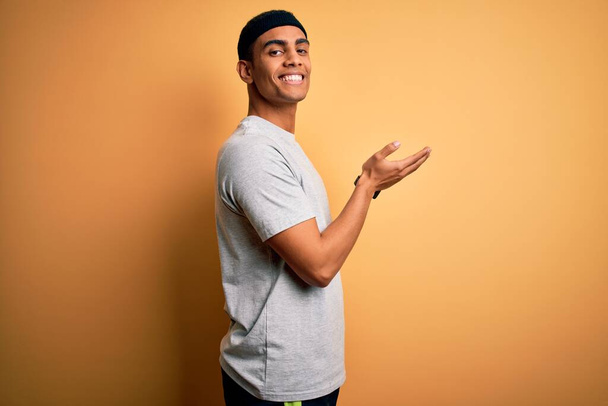 Handsome african american sportsman doing sport wearing sportswear over yellow background pointing aside with hands open palms showing copy space, presenting advertisement smiling excited happy - Photo, Image