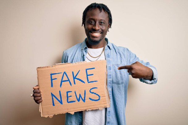 Молодий афроамериканець тримає прапор з фальшивою звісткою новин на білому тлі з несподіваним обличчям, вказуючи пальцем на себе. - Фото, зображення