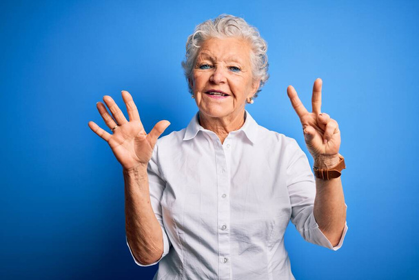 Senior bella donna indossa camicia elegante in piedi sopra isolato sfondo blu mostrando e indicando con le dita numero sette, mentre sorridente fiducioso e felice
. - Foto, immagini
