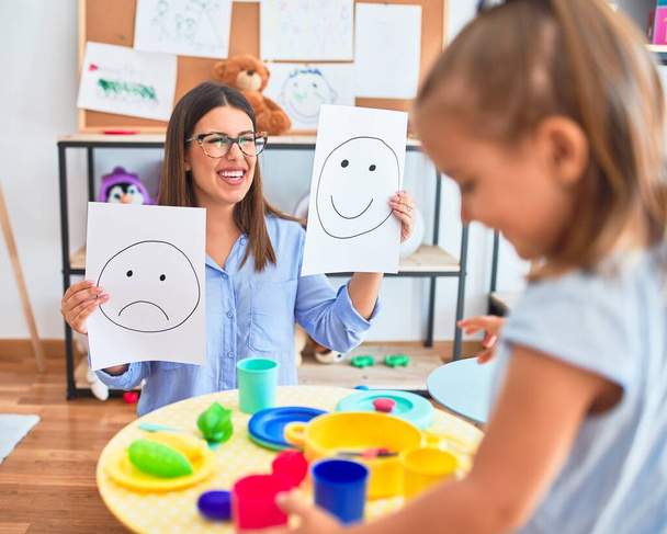 Young therapist woman speaking and treating child, counselor and behaviour correction at pedagogue payroom showing happy and sad faces - 写真・画像