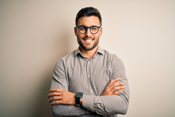 Young handsome man wearing elegant shirt and glasses over isolated white background happy face smiling with crossed arms looking at the camera. Positive person. - Foto, Bild