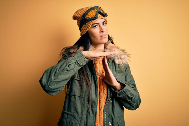 Mladá krásná hispánská žena v lyžařských brýlích a kabátě na zimní počasí dělá gesto s rukama, frustrovaný a vážný obličej - Fotografie, Obrázek