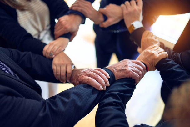 Grupo de empresários de pé em um círculo fazendo símbolo com as mãos e braços juntos no escritório
. - Foto, Imagem