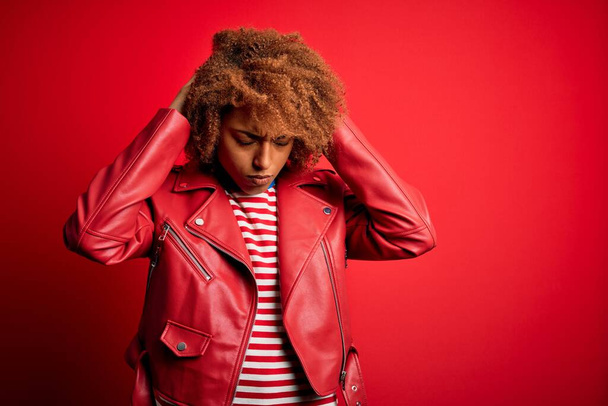 Jonge mooie Afro-Amerikaanse afro vrouw met krullend haar draagt casual rode jas die lijdt aan hoofdpijn wanhopig en gestrest omdat pijn en migraine. Handen op het hoofd. - Foto, afbeelding