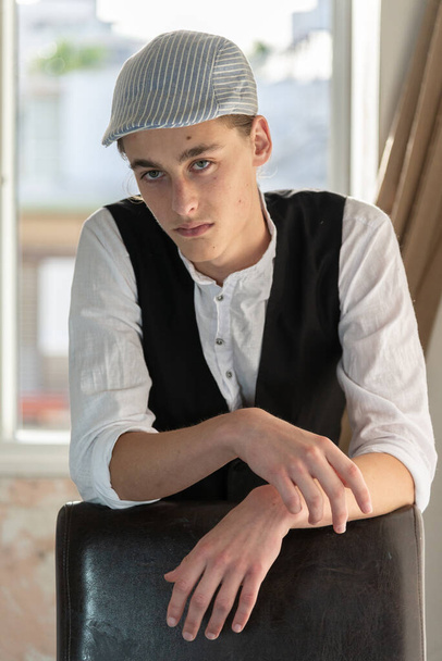 A young man in a cap and vest smokes by the window - Foto, Bild