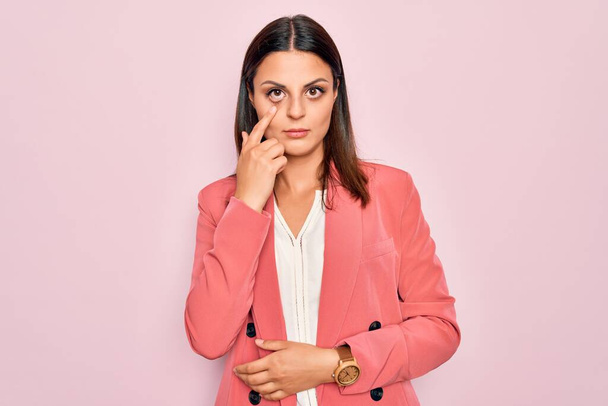 Young beautiful brunette businesswoman wearing elegant jacket over isolated pink background Pointing to the eye watching you gesture, suspicious expression - Foto, immagini