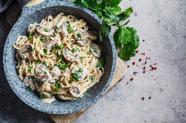 Spaghetti pasta with creamy sauce, mushrooms and parsley in a gray pan, gray background. - Foto, Imagem