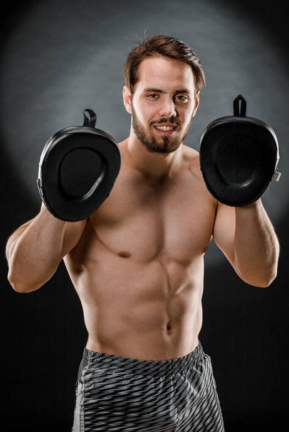 El boxeador es un luchador, mirando furiosamente a la cámara. Joven modelo de fitness masculino caucásico aislado sobre fondo negro. - Foto, imagen