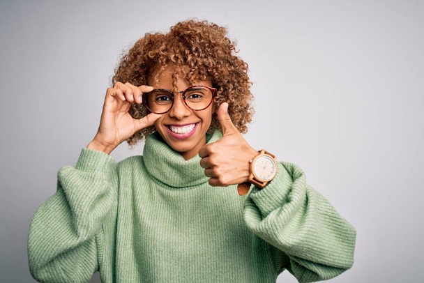 Afro-Amerikaanse optische vrouw met krullend haar dragen bril over geïsoleerde witte achtergrond blij met grote glimlach doet ok teken, duim omhoog met vingers, uitstekend teken - Foto, afbeelding