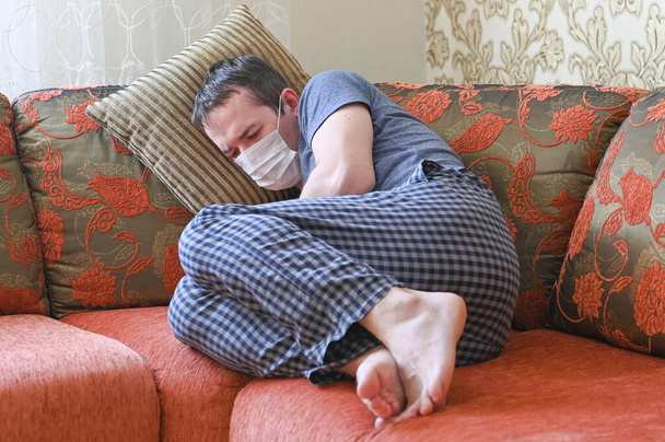 Ο άρρωστος με την προστατευτική μάσκα είναι ξαπλωμένος στον καναπέ. Αυτοαπομόνωση κατά τη διάρκεια της καραντίνας. επιδημία γρίπης, κρυολογήματα, έννοια COVID-19. - Φωτογραφία, εικόνα