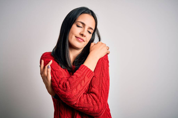 Young brunette woman with blue eyes wearing casual sweater over isolated white background Hugging oneself happy and positive, smiling confident. Self love and self care - Fotoğraf, Görsel