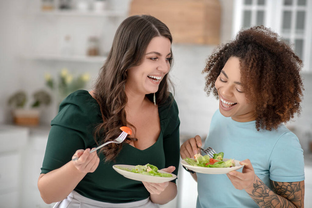 Laughing good looking women eating vegetable salad. - Фото, изображение