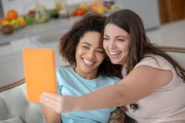 Two young cheerful girlfriends taking selfie on a tablet. - Photo, Image