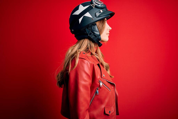 Young beautiful brunette motrocyclist woman wearing moto helmet over red background looking to side, relax profile pose with natural face with confident smile. - Fotó, kép