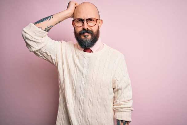 Jóképű kopasz férfi szakállal és tetoválással szemüveget visel és pulóvert rózsaszín háttér zavaros és csoda a kérdés. Kétségbeesetten, kéz a kézben gondolkodva. Töprengő koncepció. - Fotó, kép