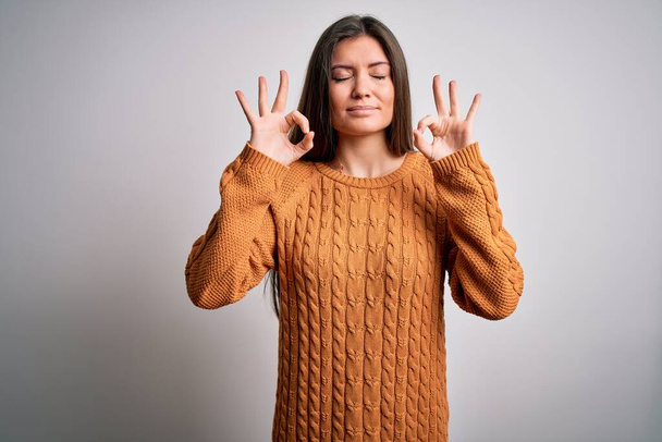 Young beautiful woman with blue eyes wearing casual sweater standing over white background relaxed and smiling with eyes closed doing meditation gesture with fingers. Yoga concept. - Fotografie, Obrázek