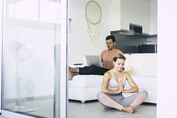 Zamknięcie kwarantanny pobyt w domu aktywność styl życia z młodą pogodną szczęśliwą kobietą zrobić jogi sportowej sesji na podłodze i chłopak usiąść z laptopem w tle - Zdjęcie, obraz