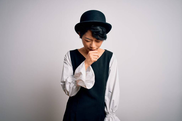 Mladá krásná asijská dívka na sobě ležérní šaty a klobouk stojící nad izolované bílé pozadí pocit nevolnosti a kašel jako symptom pro nachlazení nebo zánět průdušek. Koncept zdravotní péče. - Fotografie, Obrázek