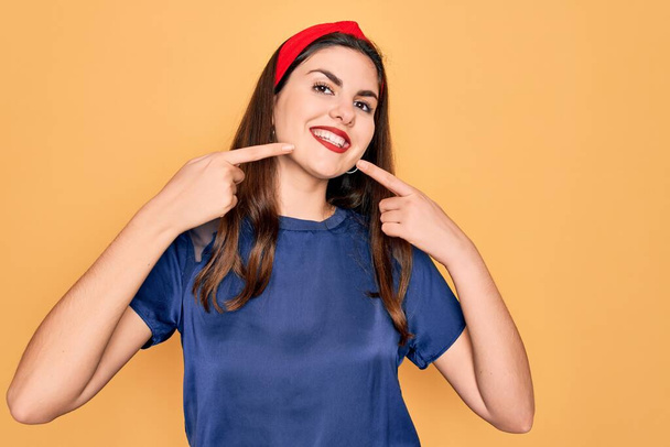 Young beautiful brunette woman wearing red lips over yellow background smiling cheerful showing and pointing with fingers teeth and mouth. Dental health concept. - Photo, Image