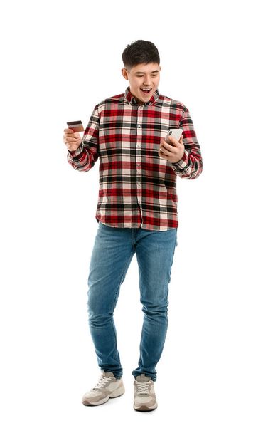 Happy Asian man with credit card and mobile phone on white background - Fotó, kép
