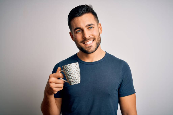 Young handsome man drinking a cup of hot coffee over white isolated background with a happy face standing and smiling with a confident smile showing teeth - Φωτογραφία, εικόνα