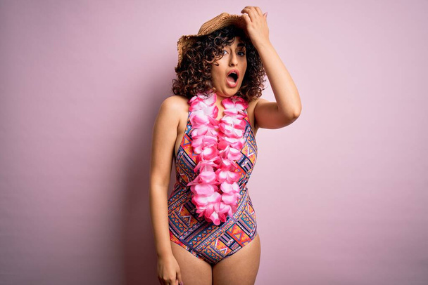 Young beautiful arab woman on vacation wearing swimsuit and hawaiian lei flowers surprised with hand on head for mistake, remember error. Forgot, bad memory concept. - Valokuva, kuva