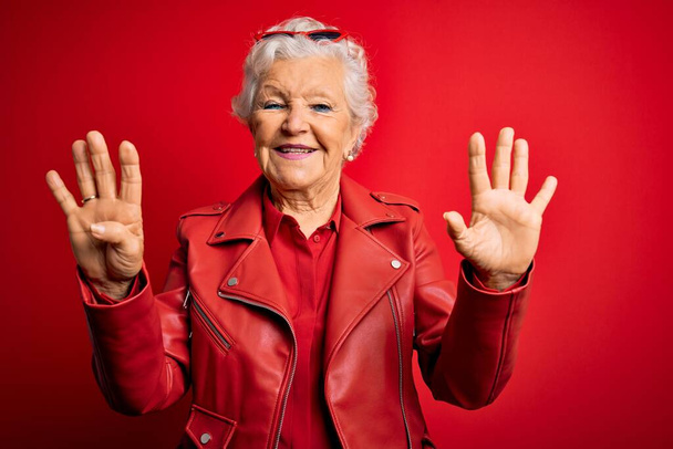 Senior schöne grauhaarige Frau trägt lässig rote Jacke und Sonnenbrille zeigt und zeigt mit den Fingern Nummer neun, während sie selbstbewusst und glücklich lächelt. - Foto, Bild