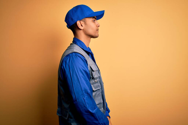 Young handsome african american handyman wearing worker uniform and cap looking to side, relax profile pose with natural face with confident smile. - Фото, изображение