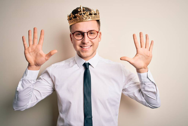 Jeune beau homme d'affaires caucasien portant la couronne d'or sur fond isolé montrant et pointant vers le haut avec les doigts numéro dix tout en souriant confiant et heureux
. - Photo, image