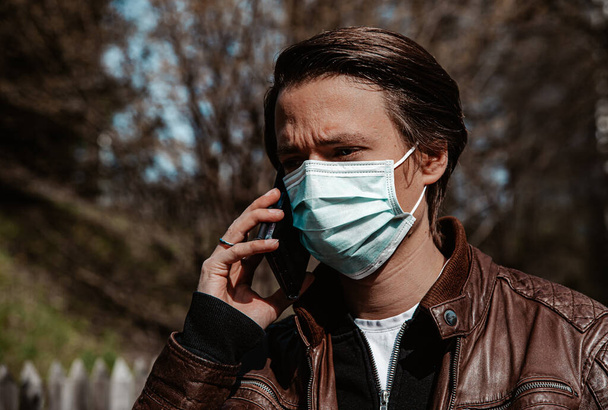 Corona - Covid-19 conceptual image - front view of a man wearing a face mask and using a cellphone - Foto, Imagem
